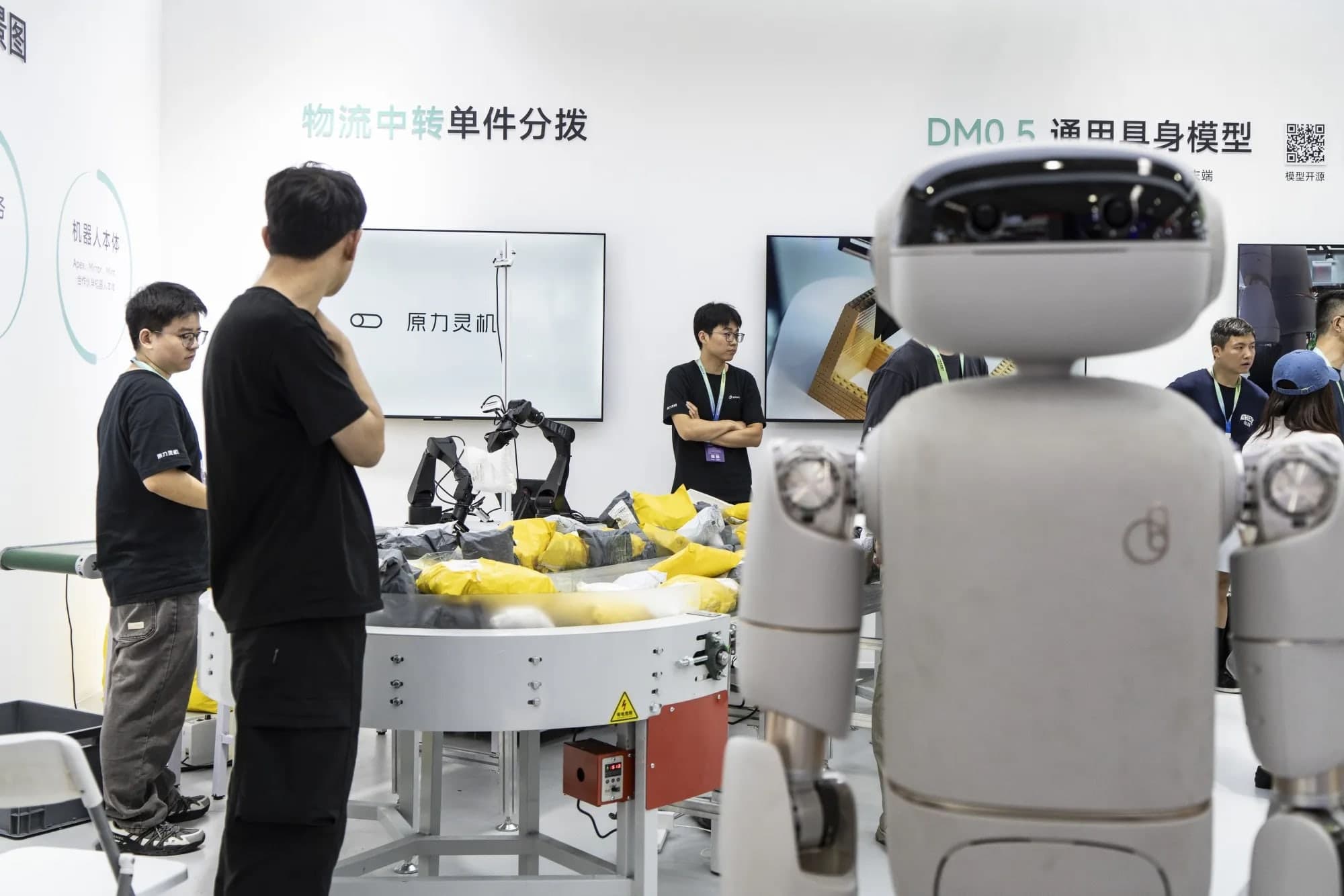 Attendees looking at robotic arms and a humanoid robot at a robotics exhibition booth with Chinese signage