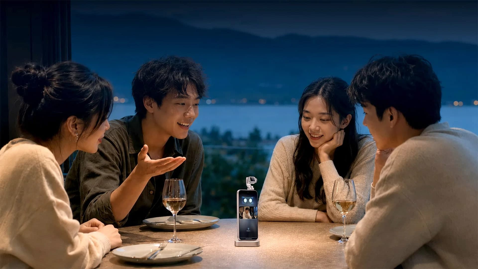 A phone with a small articulating robot arm and camera standing on a restaurant table at night while four friends talk around it