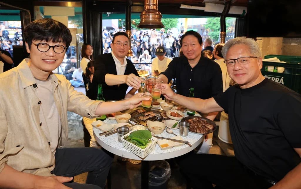 Jensen Huang and three other executives raising drinks in a toast over a Korean barbecue table crowded with photographers in the background