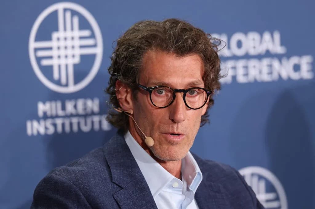 Richard Dickson wearing glasses and a headset microphone, speaking on stage in front of a Milken Institute Global Conference backdrop