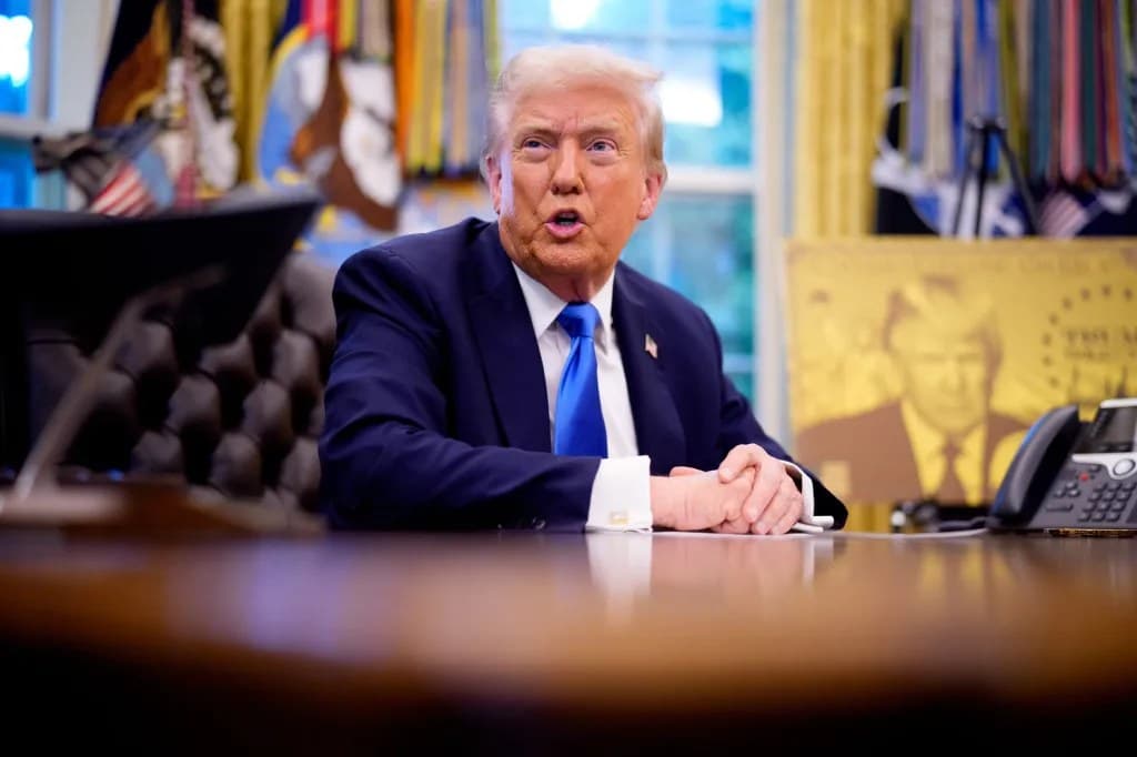 President Trump speaking from behind the Resolute Desk in the Oval Office, with hands clasped and American flags visible in the background