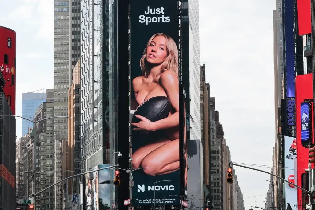 A large digital billboard in Times Square displays Novig's 'Just Sports' ad featuring Sydney Sweeney appearing nude and covering herself with a football, above the Novig logo