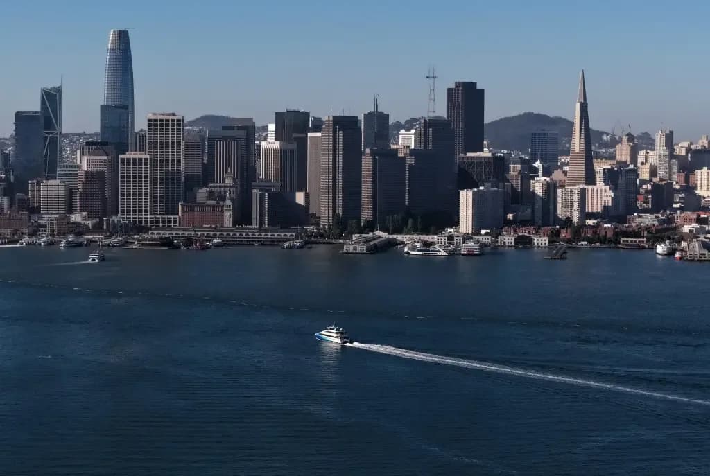 The San Francisco skyline and waterfront, including the Salesforce Tower and Transamerica Pyramid, seen across the bay with a ferry passing in front