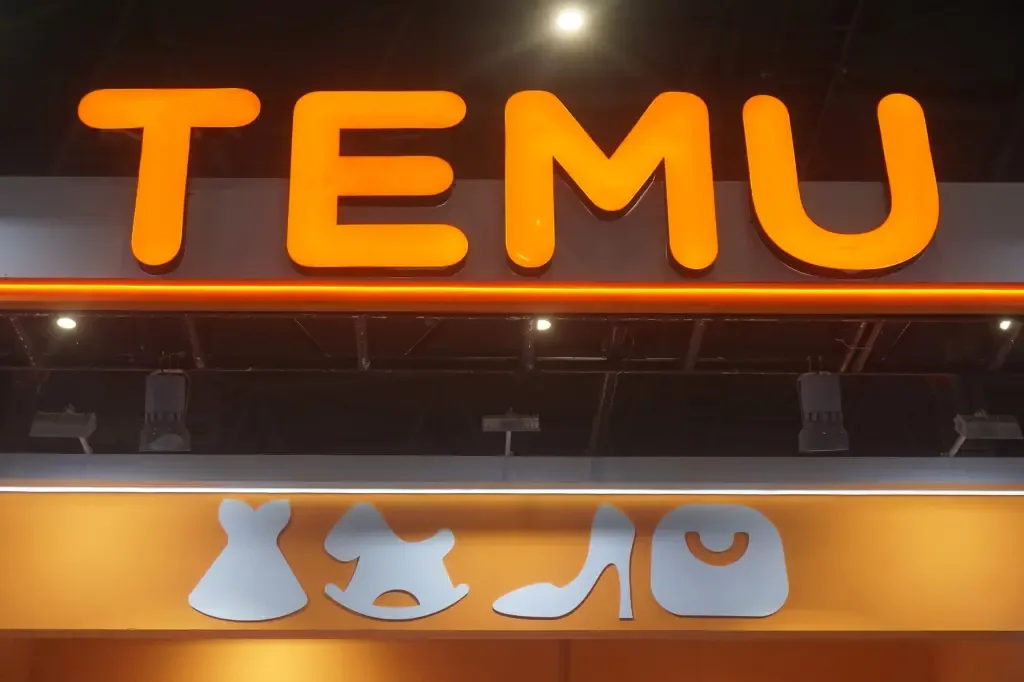 Illuminated orange TEMU signage above icons for clothing, toys, shoes, and bags at a trade show booth