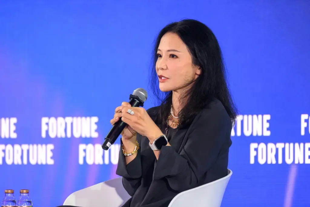 Christina Zhu speaks into a microphone while seated on stage in front of a blue Fortune-branded backdrop